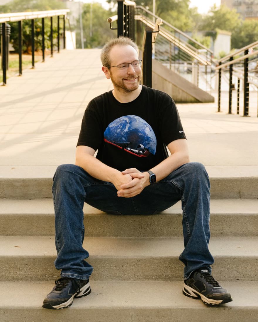 Brandon Smith sitting on concrete steps by the Milwaukee riverwalk, smiling